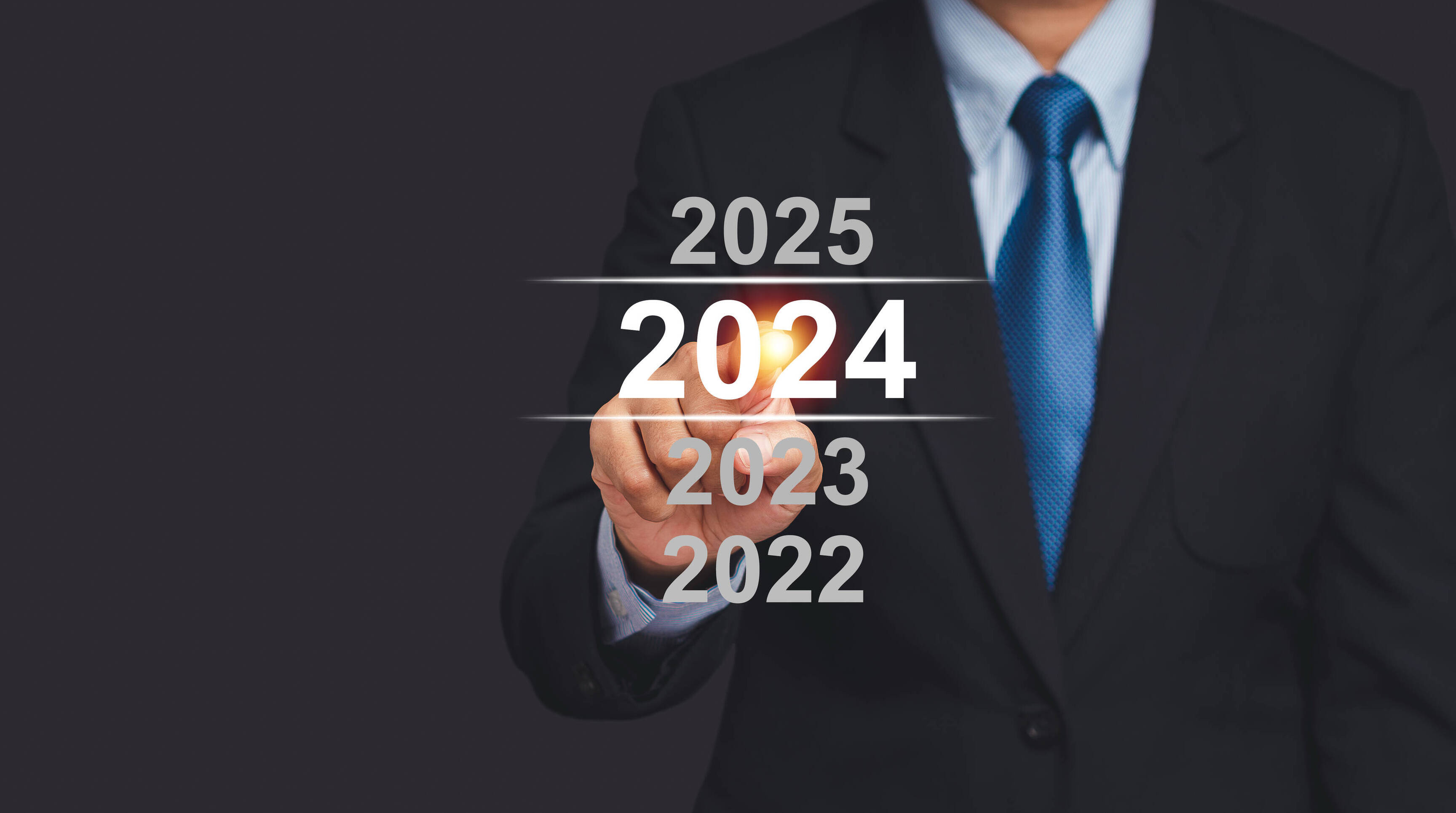A businessman in a suit points to a digital 2024 calendar on a virtual screen while standing on a black background. Countdown to 2024. New Year's Eve and changing the year 2023 to 2024